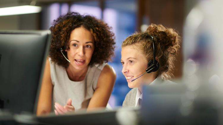 two women working on computer with headsets